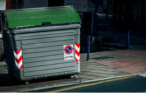 große Abfalltonne mit Containerwarnmarkierungen in der Dunkelheit am Straßenrand